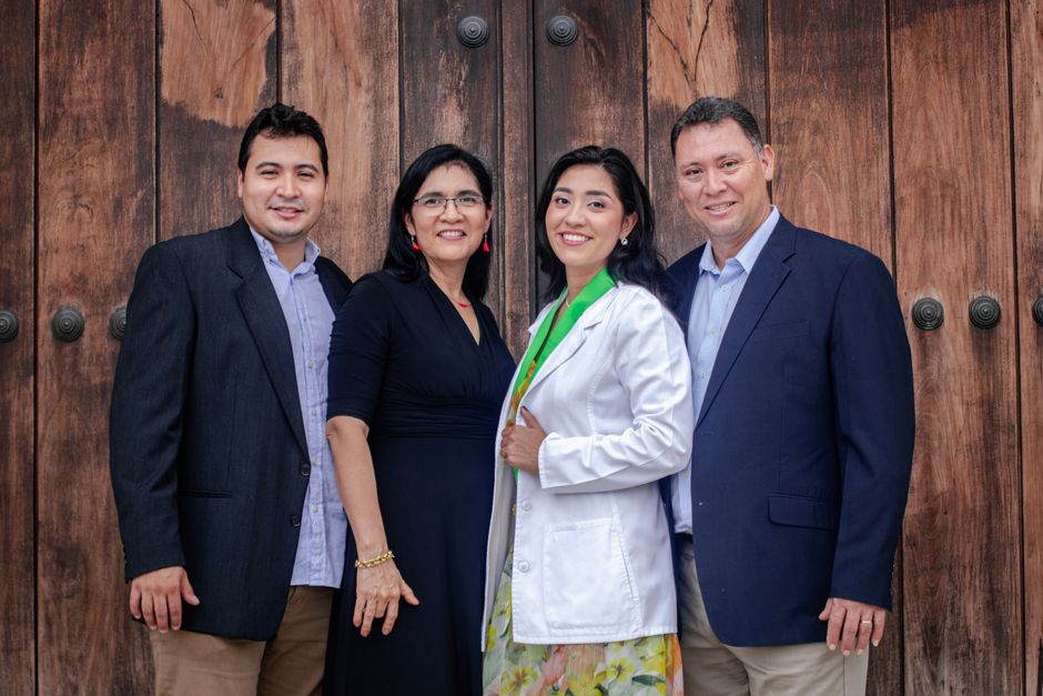 Group portrait of a smiling family in formal attire against wooden doors.